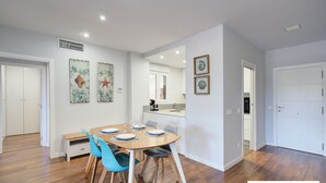 A modern dining area with a wooden table and blue chairs, a kitchen with white cabinets, and a hallway with a white door. - Ref. 565600 (Motril)