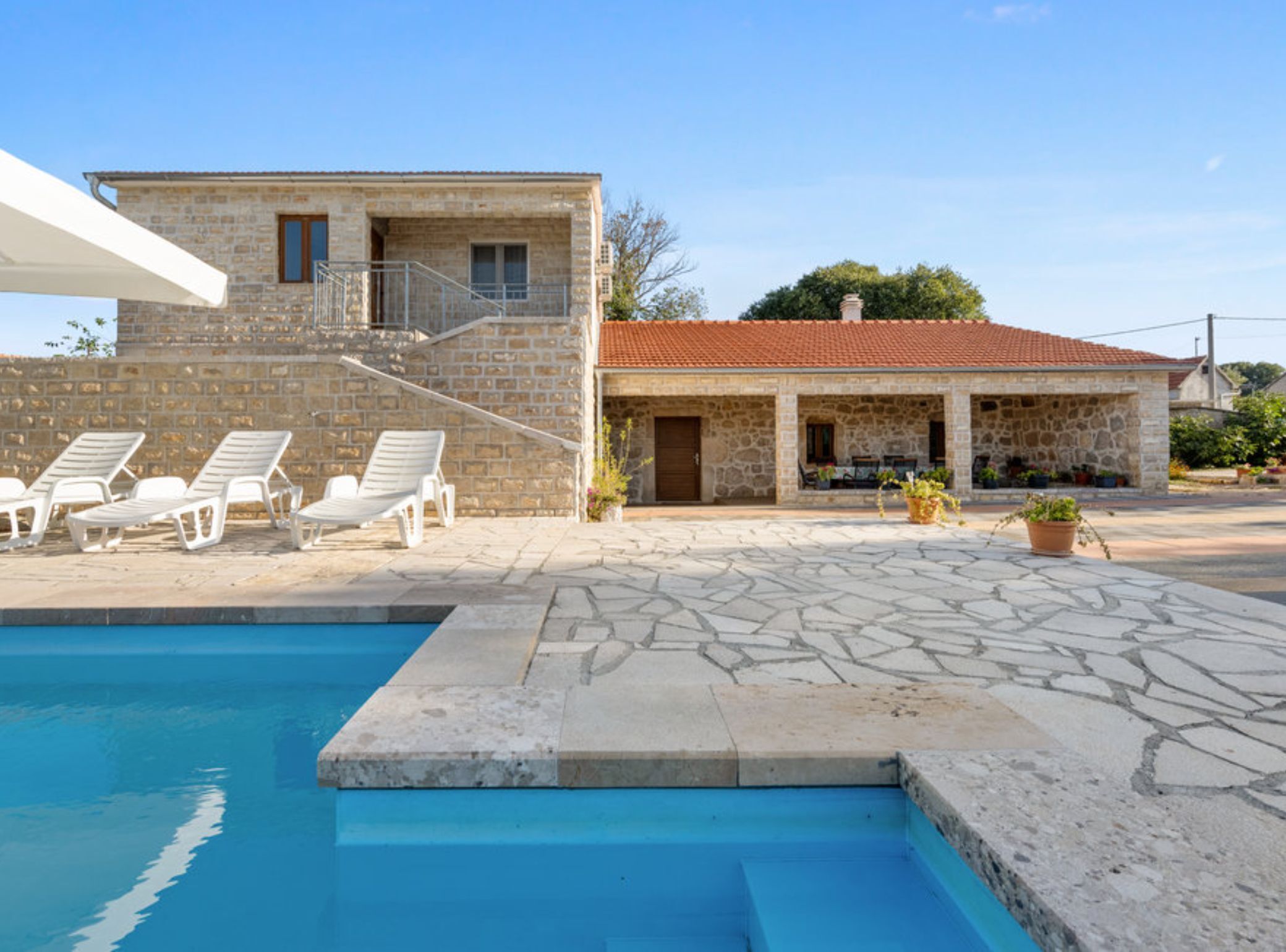 A stone house with a swimming pool, outdoor seating, and a covered patio area.