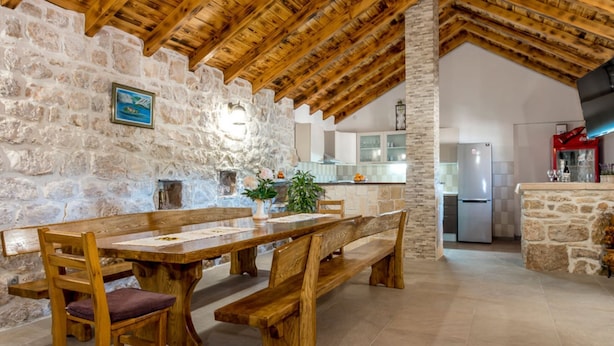 Un intérieur rustique avec des murs en pierre, des poutres en bois, un coin repas avec des bancs et une cuisine équipée d’un réfrigérateur et d’un distributeur de Coca-Cola.