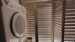 Un área de lavandería con lavadora, una puerta con persianas horizontales y piso de baldosas.