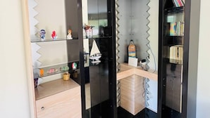 Un mueble de almacenaje moderno con múltiples compartimentos, puertas espejadas, estantes y un pequeño escritorio.