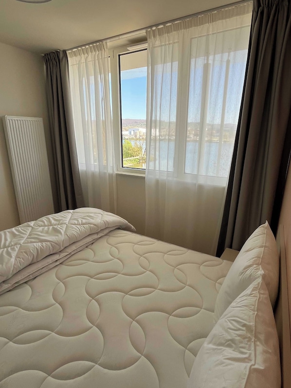 A bedroom with a bed, a window with curtains, and a radiator.