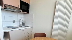 Une cuisine compacte équipée d’un four à micro-ondes, d’un évier et de placards. On y trouve une table ronde en bois avec une chaise.