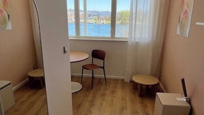 Une chambre moderne avec un grand miroir, un plancher en bois, une table ronde, une chaise et une vue sur une étendue d’eau, visible à travers de grandes fenêtres.