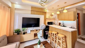 Una sala de estar moderna con una televisión de pantalla plana, muebles de madera, una mesa de centro y una zona de bar con taburetes.