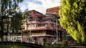 A multi-story building with balconies, a bridge, and a river in the foreground. - KINTU PLAZA HOSPEDAJE (Cuenca)