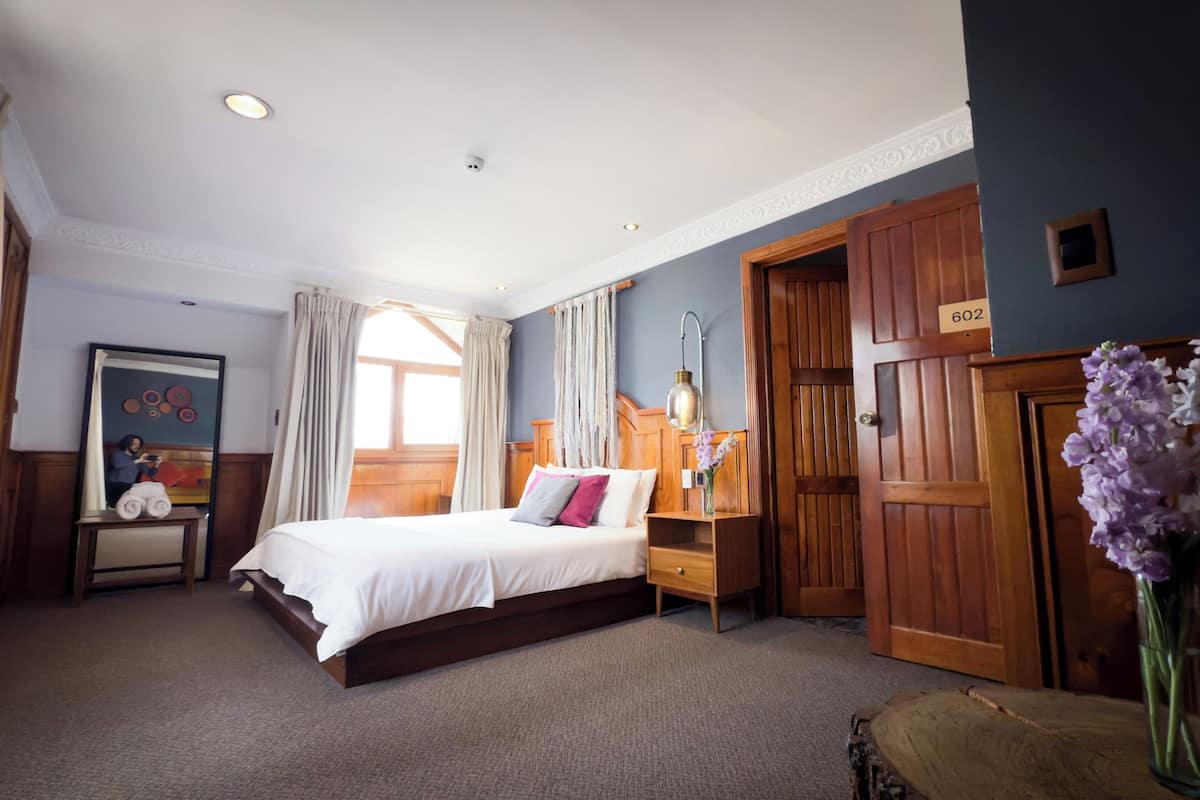 Una habitación de hotel con una cama, una mesita de noche, una lámpara, un espejo, una puerta y una ventana.