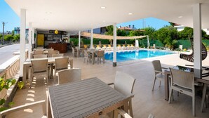 An outdoor pool area with lounge chairs, a bar, and a covered seating area. - Bova Rooms (Kemer)