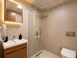 A modern bathroom with a glass-enclosed shower, a wooden vanity, a white sink, and a toilet. - Bova Rooms (Kemer)