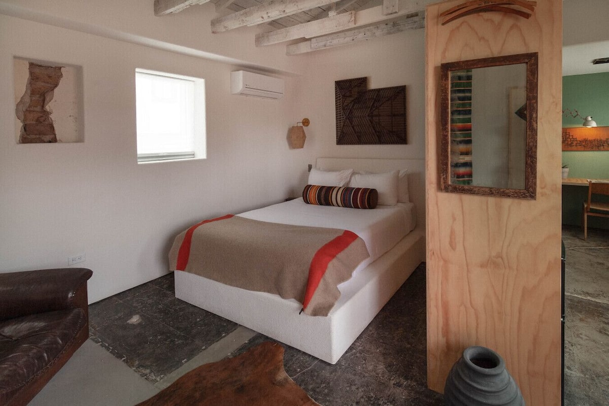 A bedroom with a bed, a wooden door, a mirror, and a window.