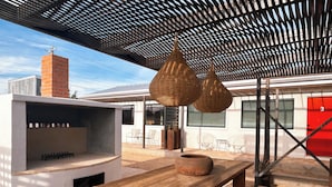 An outdoor patio with a wooden table, wicker hanging lights, and a brick chimney. - Motel Marfa (Marfa)