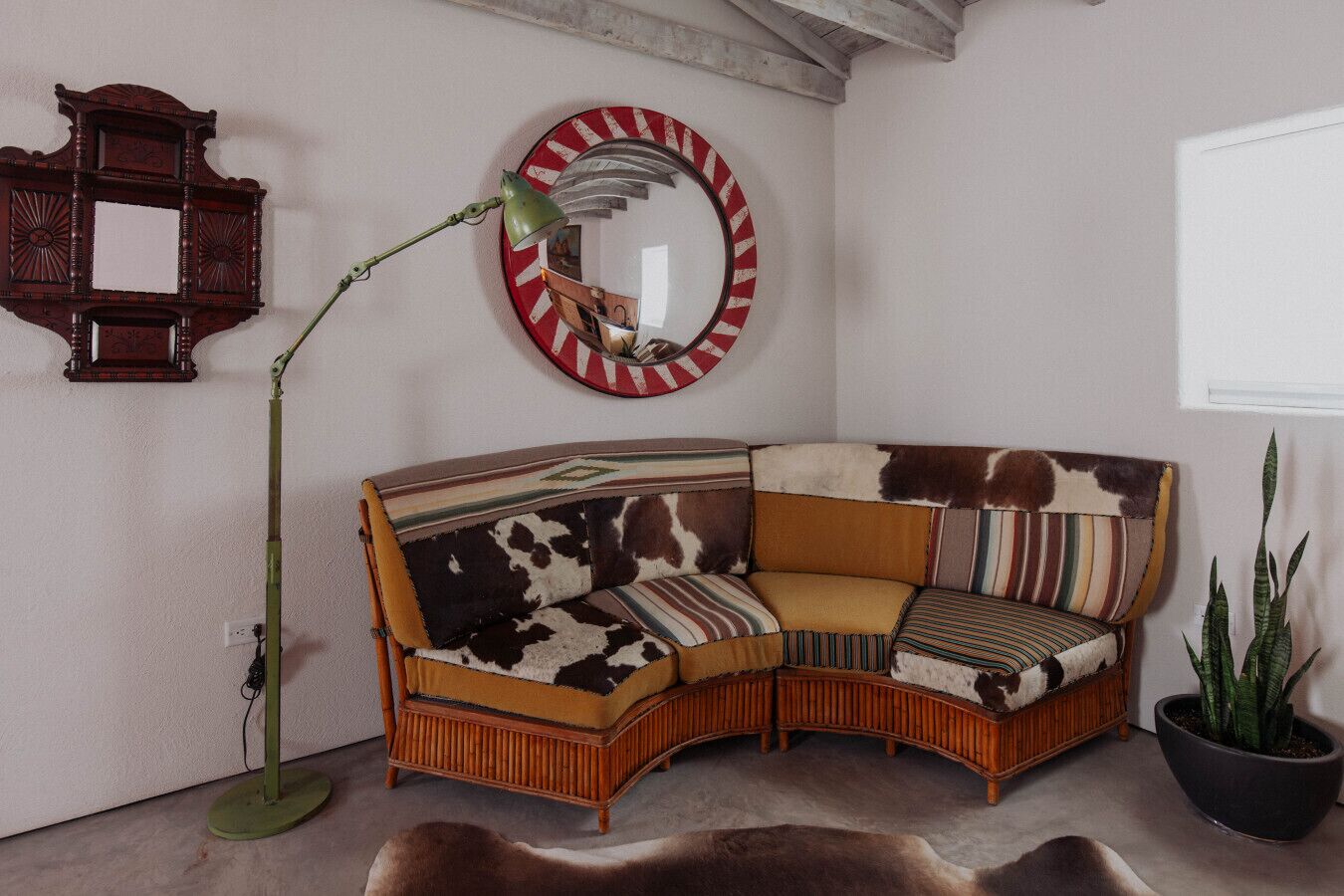 A corner sofa with a cowhide pattern, a round mirror with a red and white striped frame, a tall floor lamp, and a potted plant.