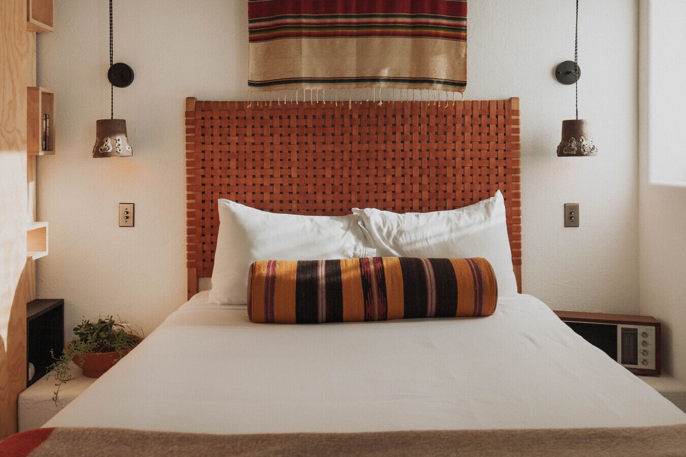 A bed with white bedding, a woven headboard, two white pillows, and a striped pillow.