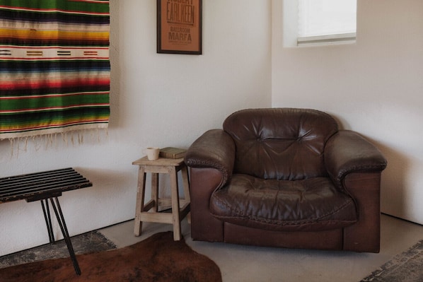 A brown leather armchair in a room with a white wall, a framed poster, a small wooden stool, and a black table. - Motel Marfa (Marfa)