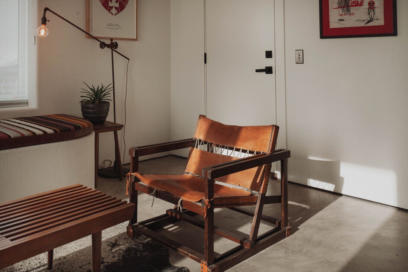 A room with a wooden bench, a leather chair, a floor lamp, and a potted plant.