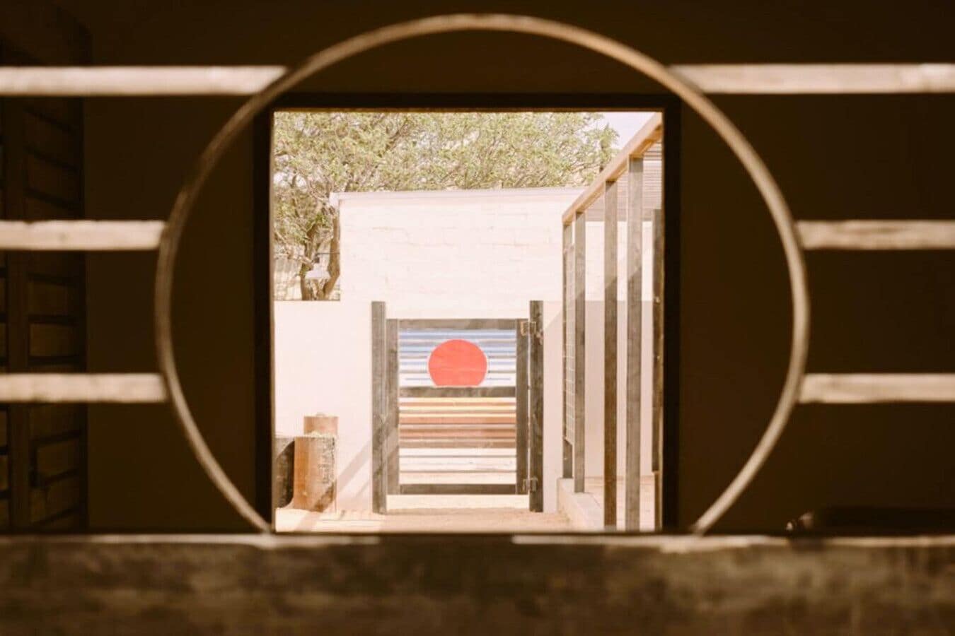 A view through a circular window with a wooden door and a red circle on the door.
