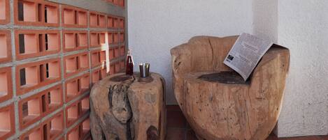 A corner with a brick wall, a wooden stool, and a wooden chair with a newspaper on it.