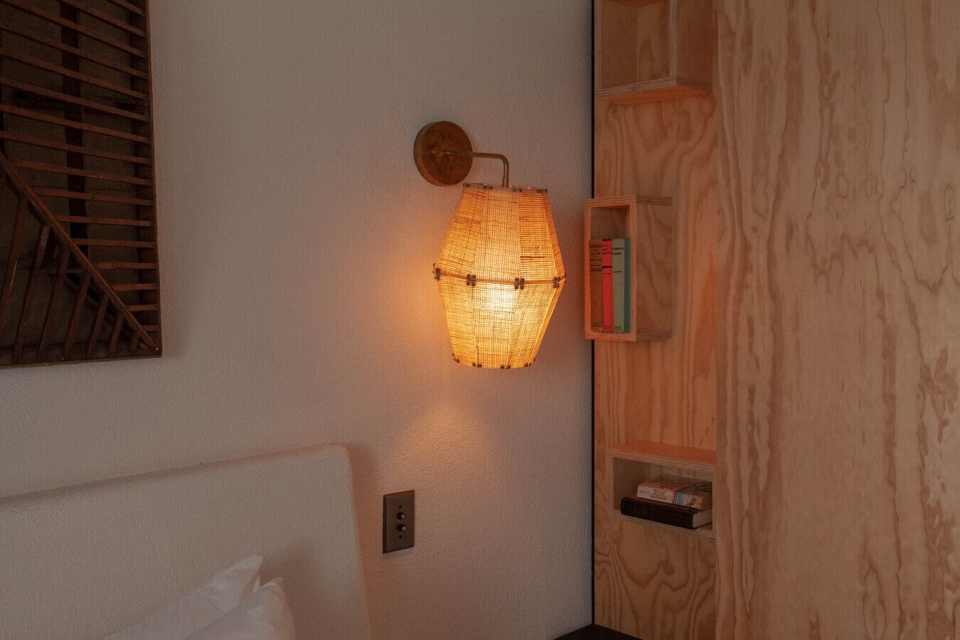 A room with a textured wall, a wall-mounted lamp, and a wooden shelf with books.