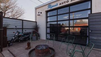 An auto shop with a large garage door, a motorcycle parked outside, and outdoor seating.