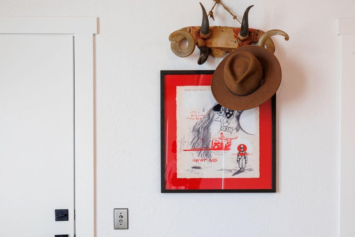 Una obra de arte enmarco con un sombrero de vaquero y una cabeza de animal con cuernos montada en una pared.