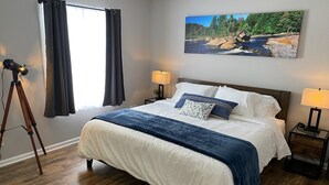 Ein ordentlich bezogenes Bett mit einer blau-weißen Bettdecke, zwei Nachttischlampen und einem Gemälde einer Flusslandschaft an der Wand.