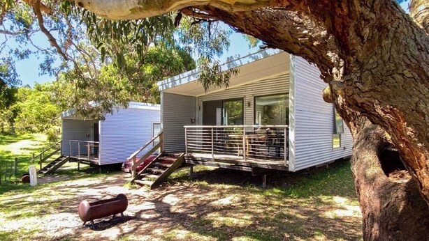 A mobile home with a balcony, a staircase, and a tree in the foreground.