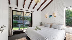 Une chambre avec un grand lit, une fenêtre donnant sur l’extérieur et un mur en briques blanches.