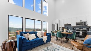 A modern living room with a blue sofa, a dining area, and a kitchen with white cabinets and stainless steel appliances. - Lux Lakeview Table Rock Branson w/ Pool & Hot Tub (Omaha)