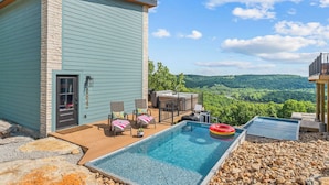 A pool with a view of the countryside, a deck with chairs, and a stone wall. - Lux Lakeview Table Rock Branson w/ Pool & Hot Tub (Omaha)