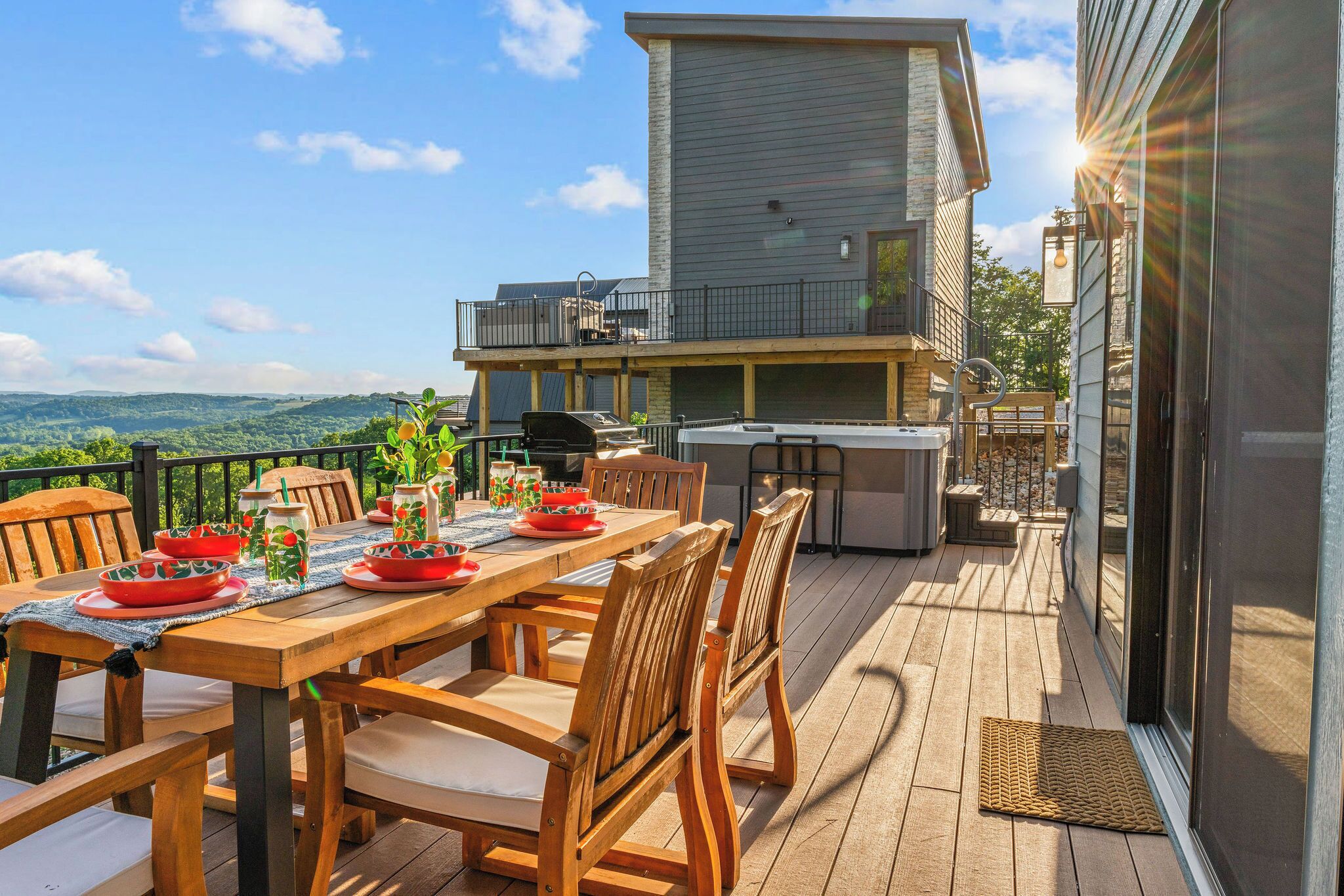 A wooden deck with a dining table set for four, outdoor furniture, and a barbecue grill.