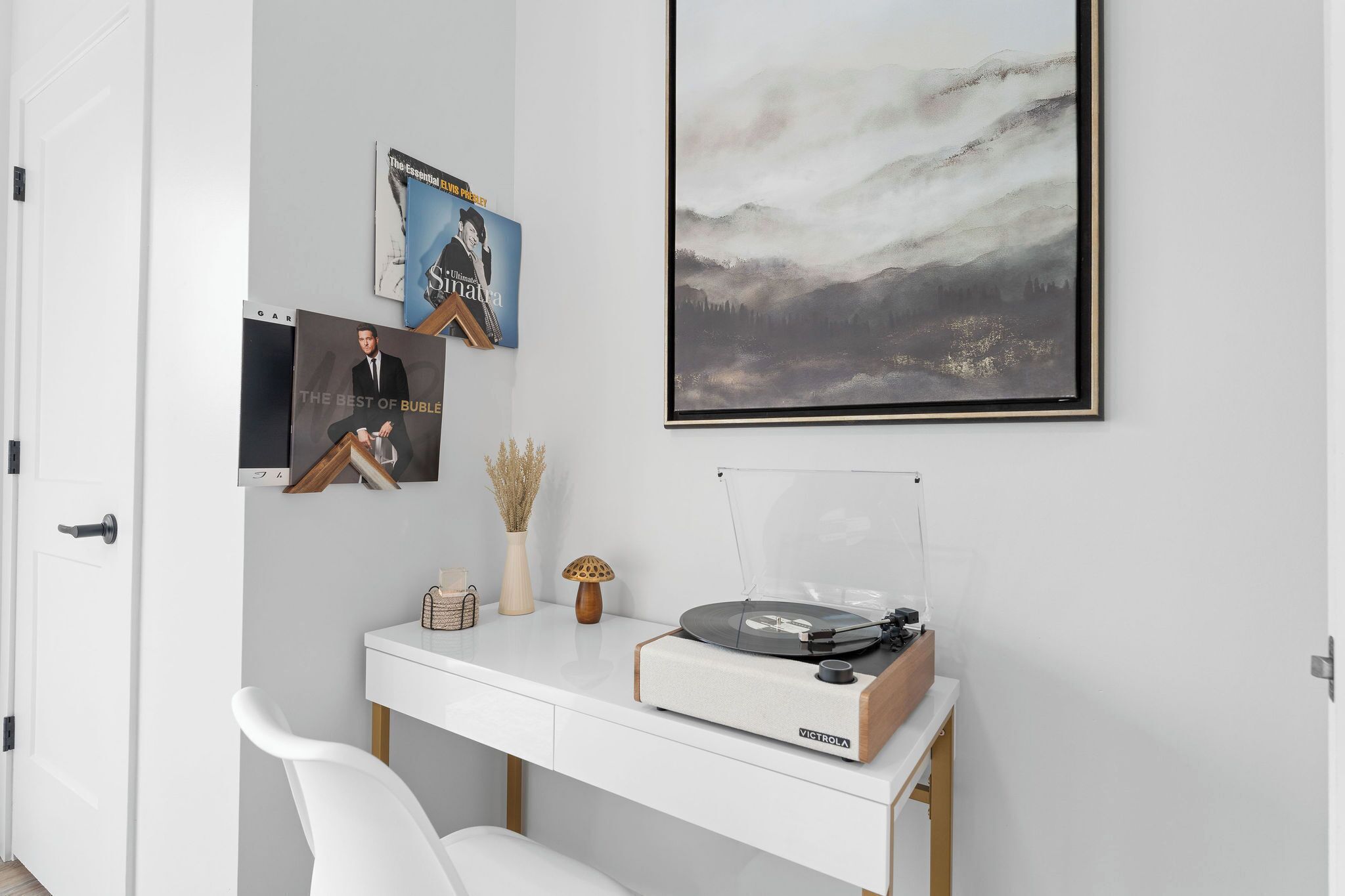 A modern room with a white desk, a turntable, and framed artwork on the wall.