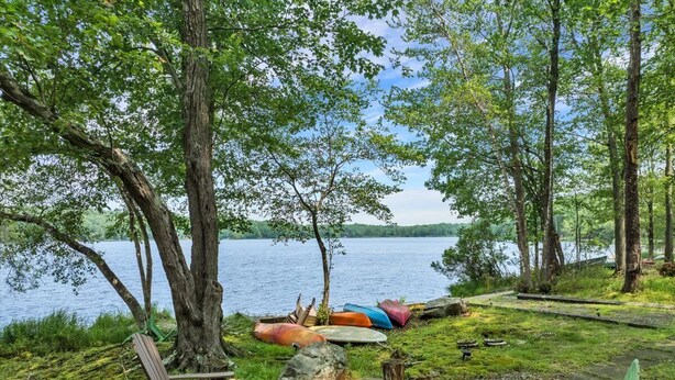 Un espace extérieur aménagé au bord du lac, avec des chaises Adirondack, un foyer et des canoës.