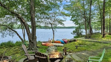 A lakeside outdoor seating area with Adirondack chairs, a fire pit, and canoes.
