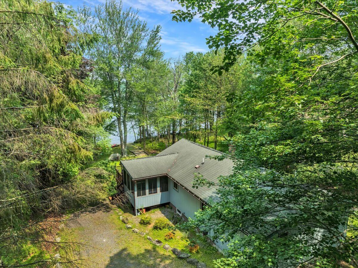 A house surrounded by dense forest with a visible deck and a small porch.