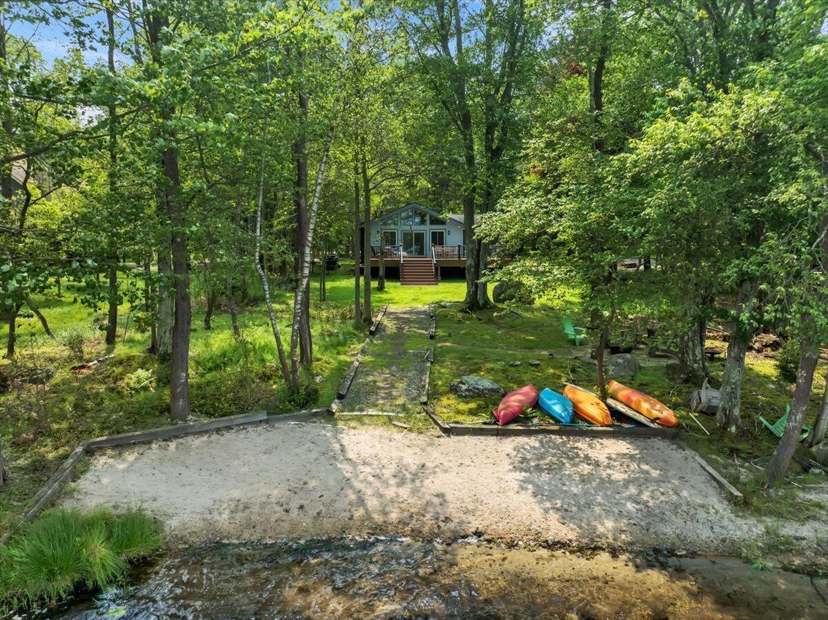 A cabin surrounded by trees with a gravel path leading to it and canoes parked nearby.