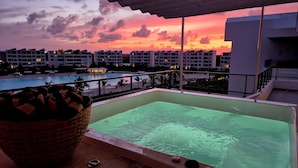 A rooftop pool with a view of a sunset and surrounding buildings. - Luxury Beach Penthouse | Whirlpool & Lagoon View | On the beach of the Crystal Lagoon (Higüey)