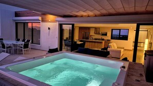 A modern outdoor living area with a hot tub, dining table, and chairs.