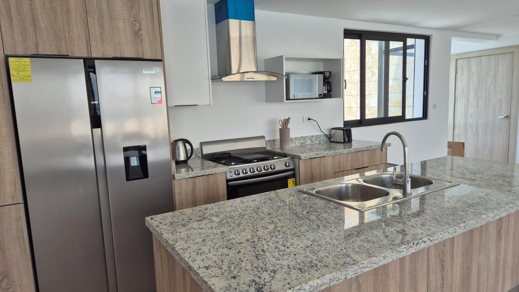 A modern kitchen with a stainless steel refrigerator, a built-in stove, and a granite countertop.
