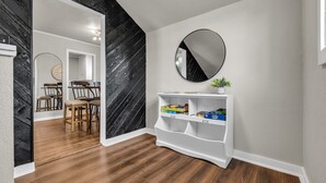 A hallway with a wooden floor, a white console table with a mirror, and a black wall with a herringbone pattern.