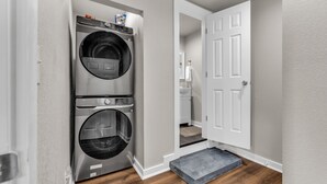 A laundry room with two stacked front-loading washers and dryers, a white door leading to a bathroom, and a small step with a gray mat at the entrance.
