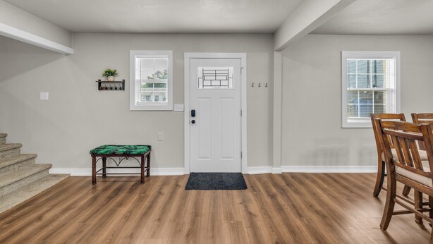 A spacious room with a wooden floor, a white door with a window, a dining table with chairs, and a small bench.
