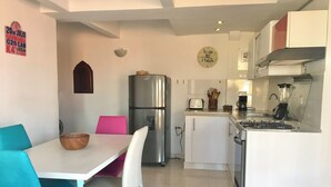 Een moderne keuken met witte kastjes, een roestvrijstalen koelkast, een gasfornuis en een inbouwoven. Er staat een eettafel met stoelen en een kom op.