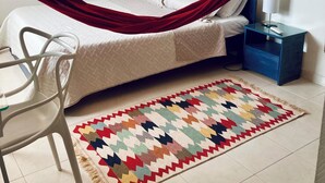 Een slaapkamer met een bed, nachtkastje, stoel, een kleurrijk vloerkleed en een rode hangmat.