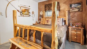 A rustic bedroom with a wooden bed frame, a small bedside table, a nightstand, and a wall-mounted shelf.