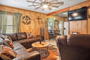 A cozy living room with a leather sofa, a wooden coffee table, and a television mounted on the wall. - The Lazy Spur | Cozy 2BR Cabin in Cowboy Capital (Bandera)