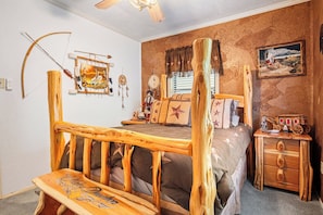 Un dormitorio de estilo rústico con cabecera de cama de madera, una banca, cómoda y adornos en la pared, incluyendo un atrapasueños y un cuadro.