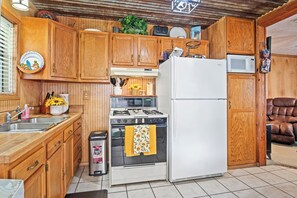 A kitchen with wooden cabinets, a stove, a refrigerator, and a trash can.