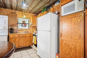 A compact kitchen with wooden cabinets, a white refrigerator, a microwave, and a stove. - The Lazy Spur | Cozy 2BR Cabin in Cowboy Capital (Bandera)