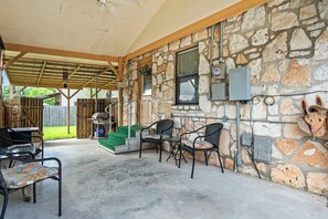 An outdoor patio with stone walls, a covered seating area, and a barbecue grill. - The Lazy Spur | Cozy 2BR Cabin in Cowboy Capital (Bandera)
