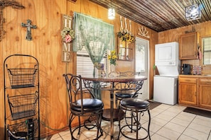 A kitchen with a wooden interior, a round dining table, two chairs, a coffee machine, and a refrigerator. - The Lazy Spur | Cozy 2BR Cabin in Cowboy Capital (Bandera)